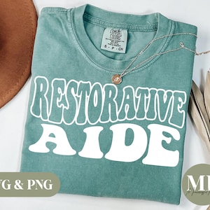 May include: A teal blue t-shirt with the text "Restorative Aide" in white, retro-style lettering. The shirt is made of a soft, comfortable material and is perfect for everyday wear.