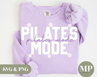 May include: Purple sweatshirt with the text "PILATES pilates mode MODE" in white with small white daisy flowers scattered around the text.