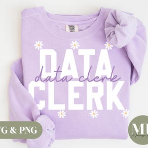 May include: A light purple sweatshirt with the words "DATA CLERK" in white block letters and "data clerk" in cursive. White daisy graphics are scattered across the front. The sweatshirt has a Comfort Colors tag.