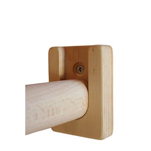 Puede incluir: Un toallero de madera natural. Cuenta con una barra cilíndrica sujeta por un soporte cuadrado, fijado con un tornillo. La madera tiene un tono claro y cálido. El diseño es sencillo y funcional, ideal para el baño.