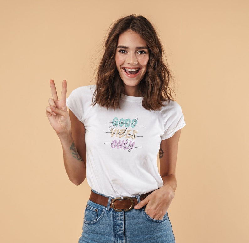 Peut inclure: Un t-shirt blanc avec le texte "GOOD VIBES ONLY" en lettres color&eacute;es. Le texte est &eacute;crit en cursive et est s&eacute;par&eacute; par des lignes.