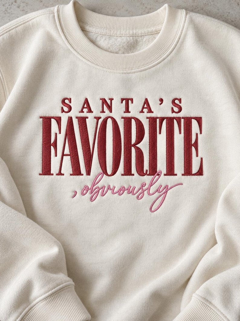 May include: A cream-colored crewneck sweatshirt featuring embroidered text on the front. The words SANTA'S FAVORITE are stitched in bold red capital letters, with the word obviously stitched below in a cursive pink script font.
