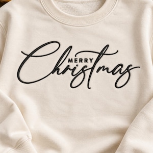 May include: A cream-colored crewneck sweatshirt featuring the black embroidered text Merry Christmas. The word Merry is printed in a simple sans-serif font, while the word Christmas is written in a large, elegant, flowing cursive script.