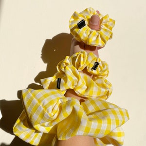 Könnte beinhalten: Drei gelbe und weiße Gingham-Scrunchies mit schwarzen Gummibändern.