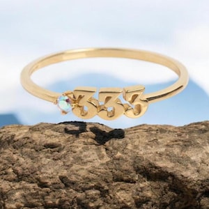 Könnte beinhalten: Goldring mit der Nummer 333 und einem kleinen schillernden Stein. Der Ring liegt auf einem braunen Stein.