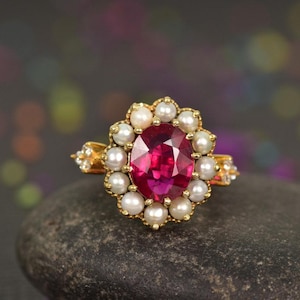 Könnte beinhalten: Ein goldener Ring mit einem großen ovalen rosafarbenen Edelstein, der von einem Heiligenschein aus weißen Perlen umgeben ist.