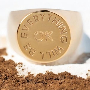 Könnte beinhalten: Ein goldener Siegelring mit der Gravur "BE EVERYTHING WILL BE OK" am Rand.