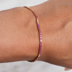 Könnte beinhalten: Ein zartes Goldarmband mit abwechselnd rosafarbenen und weißen Edelsteinen. Das Armband besteht aus einer dünnen Kette und hat ein schlichtes, elegantes Design.