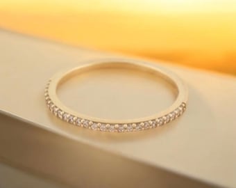 Può includere: Un sottile anello a fascia d'oro con una fila di piccole pietre trasparenti incastonate attorno all'intera fascia.
