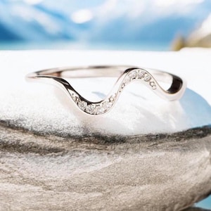 Könnte beinhalten: Ein zarter, wellenförmiger Ehering mit einer Reihe kleiner Diamanten in Weißgold.