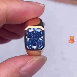 Könnte beinhalten: Ein goldener Ring mit einem großen, quadratischen blauen Edelstein.