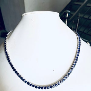 Puede incluir: Un collar de cadena de plata con piedras preciosas azules. El collar est&aacute; en un busto de maniqu&iacute; blanco.