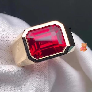 May include: A gold ring with a large, emerald-cut ruby gemstone. The ring has a thick band and a polished finish.