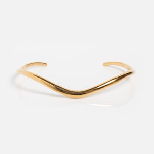 Könnte beinhalten: Ein goldfarbenes Armreif-Armband mit V-förmigem Design. Das Armband hat eine glatte, polierte Oberfläche und eine minimalistische Ästhetik. Das offene Design ermöglicht ein einfaches Tragen.