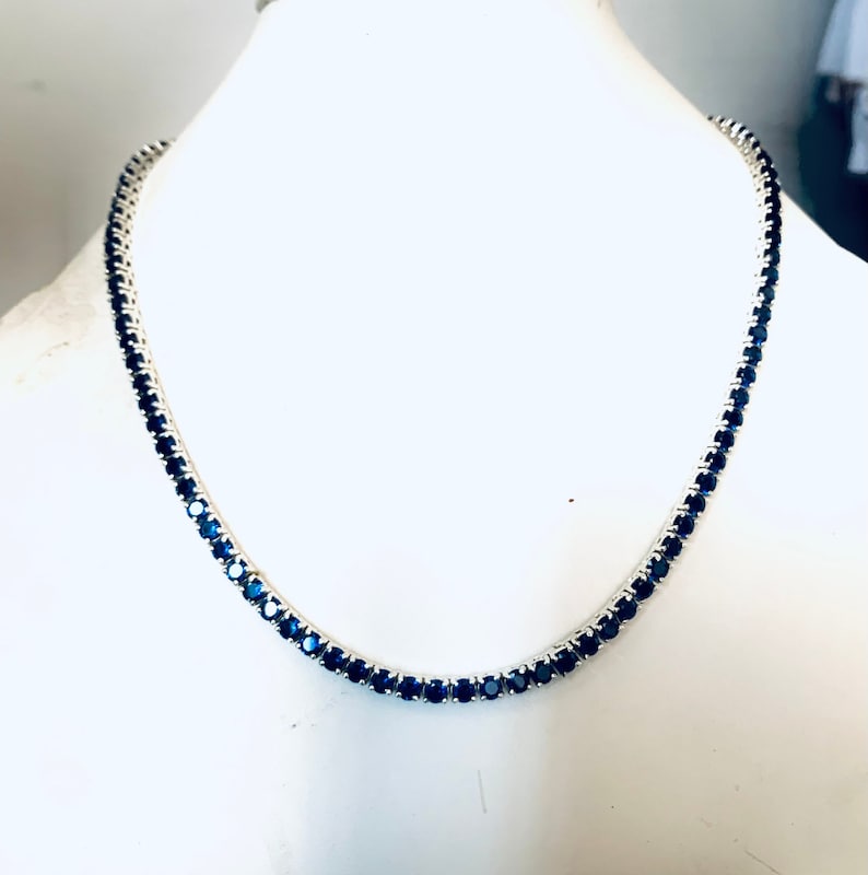 Puede incluir: Un collar de cadena de plata con piedras redondas de color azul oscuro engastadas en pav&eacute;.