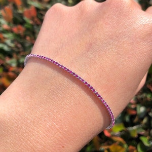 Könnte beinhalten: Ein zartes Tennisarmband mit einer Reihe kleiner rosafarbener Edelsteine, die in einem silbernen Band gefasst sind.