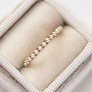 Puede incluir: Un delicado anillo de banda de oro con una fila de pequeñas perlas blancas.