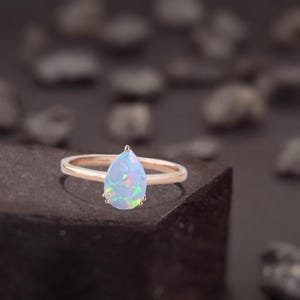 Könnte beinhalten: Ein Ring mit einem birnenförmigen Opal, der in Roségold gefasst ist. Der Opal ist hellblau mit schillernden grün, rosa und orangefarbenen Blitzen.