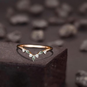 Könnte beinhalten: Ein zarter Roségold-Ehering mit geschwungenem Design und kleinen, klaren Edelsteinen. Der Ring liegt auf einer dunkelgrauen Oberfläche.