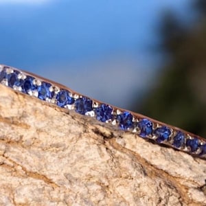 May include: A delicate silver band ring with a row of small, sparkling blue sapphires.