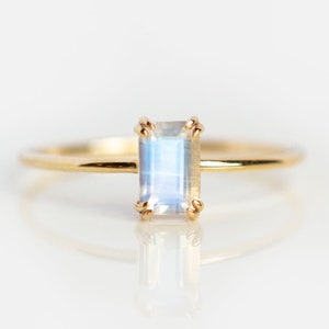 Puede incluir: Un anillo de oro con una piedra de luna rectangular transparente.