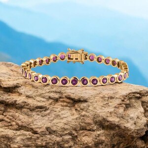 Könnte beinhalten: Ein goldenes Armband mit einer Reihe kleiner, runder, lila Edelsteine.