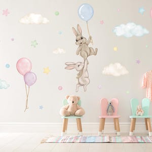 K&ouml;nnte beinhalten: Ein Wandaufkleber-Set f&uuml;r Kinderzimmer mit Hasen, die Ballons, Wolken und Sterne halten. Die Aufkleber sind in Pastellfarben gehalten und perfekt f&uuml;r ein Babyzimmer.