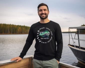 Puede incluir: Una camiseta negra de manga larga con un estampado gráfico blanco en forma de círculo que contiene la palabra "ICELAND". El círculo está rodeado de una lista de atracciones islandesas, incluyendo glaciares, cascadas, volcanes y auroras boreales. El texto "JONES FAMILY TRIP 2015" también está incluido en el gráfico.