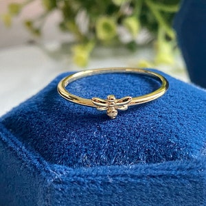 Könnte beinhalten: Ein goldener Ring mit einem Bienen-Design. Der Ring liegt auf einem blauen Samtkästchen.