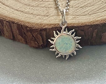 Puede incluir: Un collar de plata con un colgante de sol con una piedra de ópalo blanco.