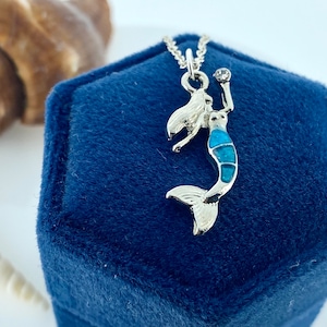 May include: A silver mermaid pendant necklace with a blue and green enamel design. The necklace is in a blue velvet box.