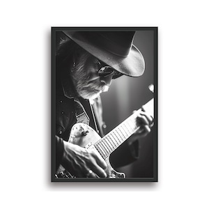 Puede incluir: Una fotografía en blanco y negro de un hombre con sombrero y gafas de sol tocando una guitarra. El hombre está enfocado, mientras que el fondo está desenfocado.