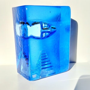 May include: A striking blue glass sculpture featuring a fish design and a textured finish. The rectangular sculpture has a fish motif and a pyramid-like structure. The base of the sculpture has the text "KOSTA BODA".