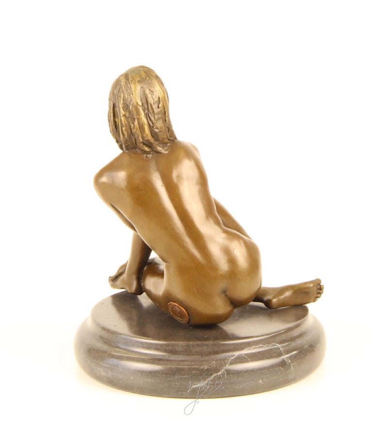 May include: Bronze sculpture of a seated figure, viewed from the back. The figure is positioned on a dark, circular base. The sculpture has a smooth, polished finish, with details in the hair and form.