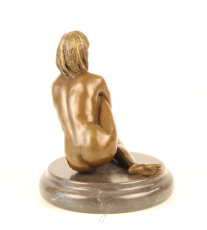 May include: A bronze sculpture of a seated figure, viewed from the back. The figure is positioned on a round, marble-like base. The sculpture has a smooth, polished finish and is set against a white background.