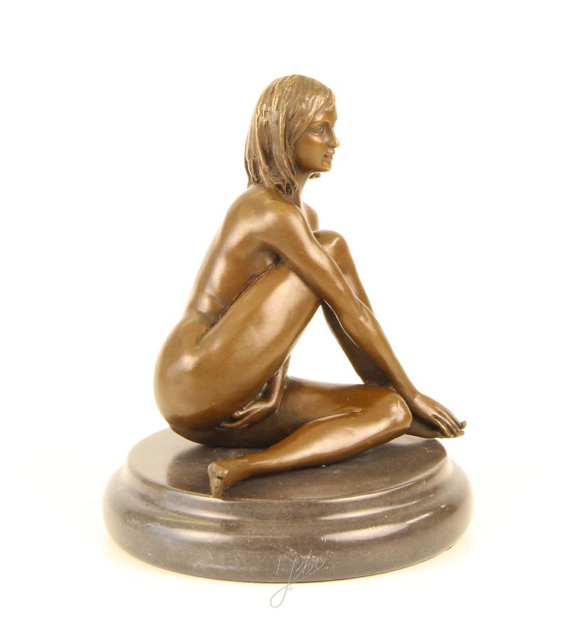 May include: A bronze sculpture of a seated figure with short hair, resting on a round, dark gray base. The figure is nude, with arms and legs crossed. The sculpture has a smooth, polished finish and is set against a white background.