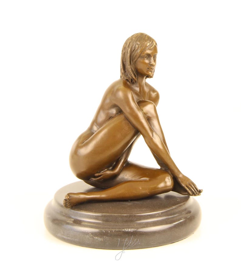 May include: Bronze sculpture of a seated figure with a serene expression. The figure is posed with one leg bent and the other extended, resting on a circular base. The sculpture has a smooth, polished finish and is set against a white background.