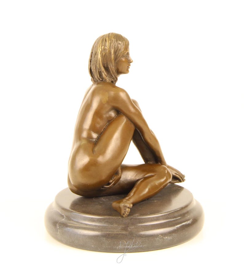 May include: Bronze sculpture of a seated figure with short hair, resting on a round, dark base. The figure is nude, with arms and legs crossed. The sculpture has a smooth, polished finish and is set against a white background.