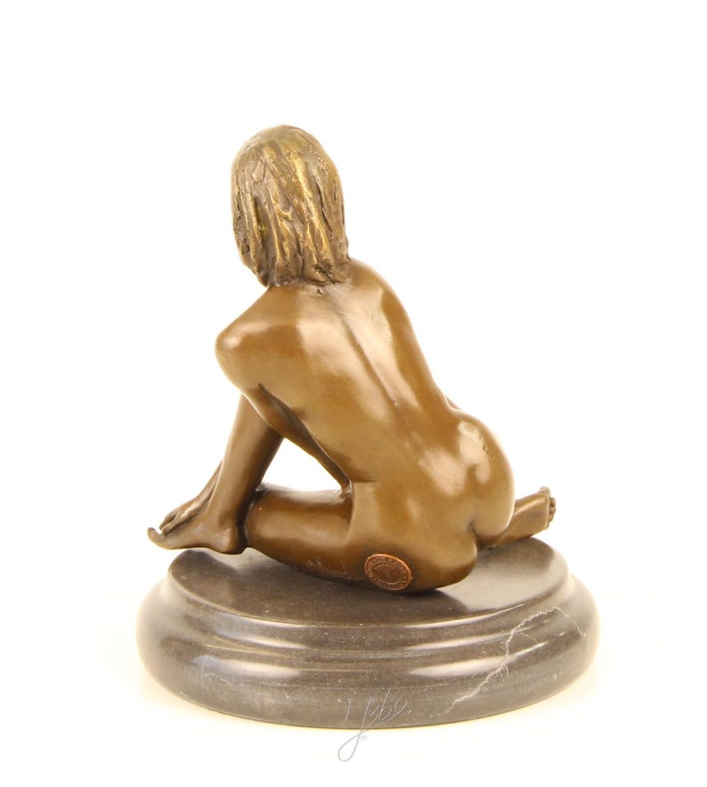 May include: Bronze sculpture of a seated figure, viewed from the back. The figure has short hair and is seated on a dark, round marble base. The sculpture has a smooth, polished finish.