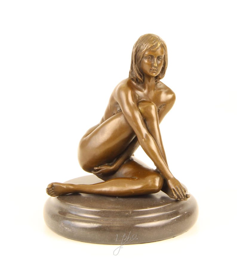 May include: Bronze sculpture of a seated figure with crossed arms and legs. The figure is positioned on a dark, circular base. The sculpture has a smooth, polished finish and is set against a white background.
