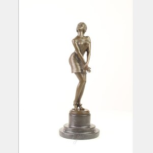 Könnte beinhalten: Bronzeskulptur einer Frau in einem kurzen Kleid, die auf einem schwarzen Marmorsockel steht. Die Frau blickt nach oben und ihre Hände sind vor ihr gefaltet.