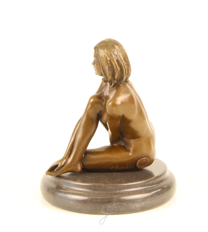 May include: Bronze sculpture of a seated figure with short hair, resting on a dark, circular base. The figure is in a relaxed pose, with one leg bent and the other extended. The sculpture has a smooth, polished finish.