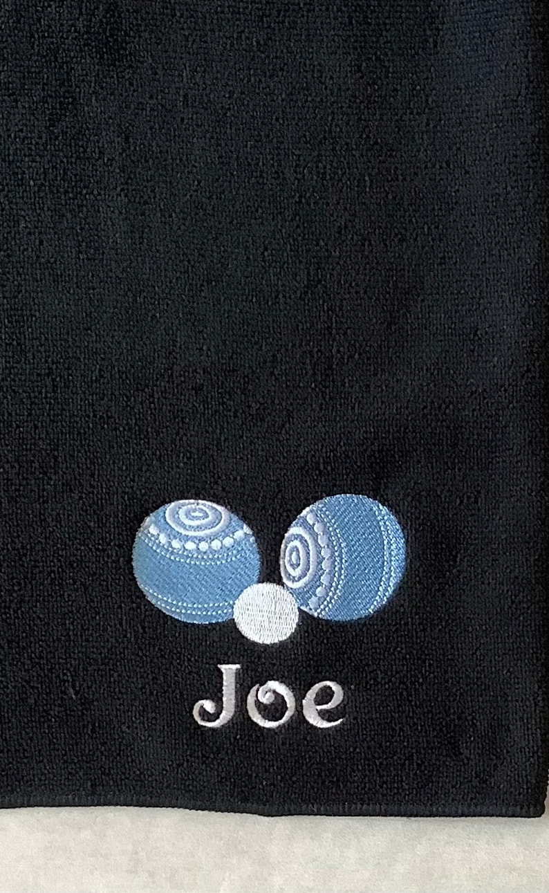 K&ouml;nnte beinhalten: Schwarzes Handtuch mit zwei blauen und wei&szlig;en Bowlingkugeln und dem Namen "Joe" in wei&szlig; gestickt.