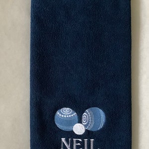 K&ouml;nnte beinhalten: Ein dunkelblaues Handtuch mit einem wei&szlig;en gestickten Design aus zwei blauen Bowlingkugeln und einer wei&szlig;en Bowlingkugel. Der Name "NEIL" ist unter den Bowlingkugeln gestickt.