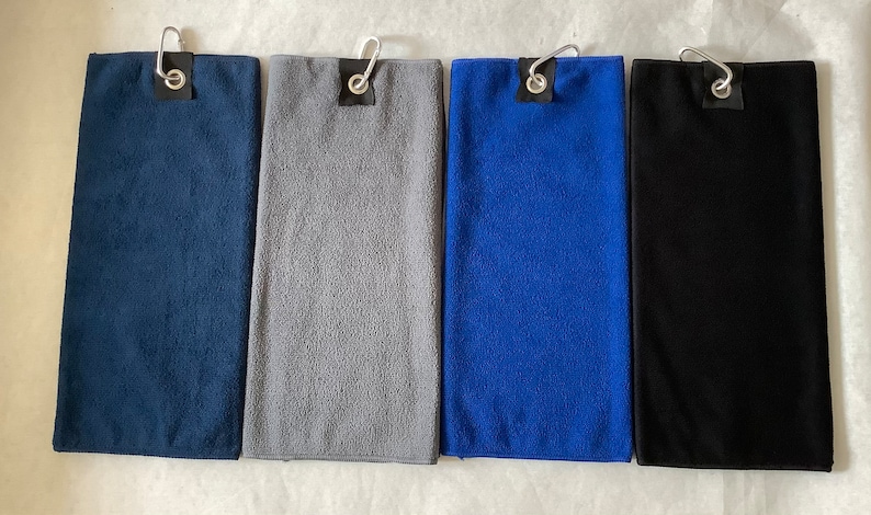 K&ouml;nnte beinhalten: Vier Mikrofaser-Golft&uuml;cher in verschiedenen Farben: marineblau, grau, royalblau und schwarz. Jedes Handtuch hat einen Metallhaken und eine schwarze Schlaufe.
