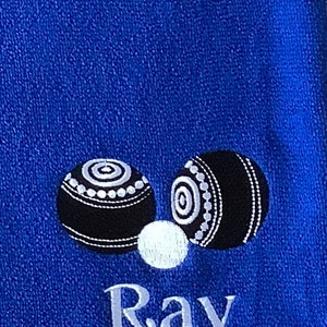 K&ouml;nnte beinhalten: Ein blaues Handtuch mit zwei wei&szlig;en und schwarzen Bowlingkugeln und dem Namen "Ray" bestickt.