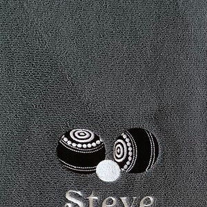 K&ouml;nnte beinhalten: Ein graues Handtuch mit zwei schwarzen und wei&szlig;en Bowlingkugeln und dem Namen "Steve", der in Wei&szlig; gestickt ist.