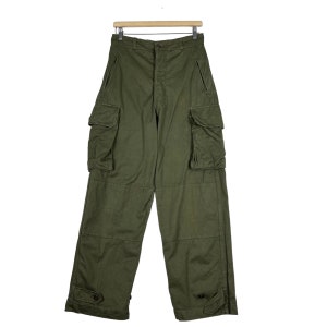May include: Olive green cargo trousers with multiple pockets on the legs. The trousers are hanging on a wooden hanger against a white background. They have a button and zip closure and buttoned cuffs at the ankles.