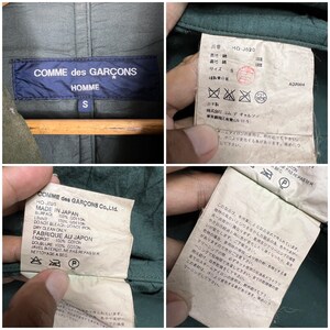 May include: Close-up of several tags from a Comme des Gar&ccedil;ons Homme garment. The tags display the brand name, size "S", and care instructions. The fabric composition is 100% cotton. The garment is made in Japan.