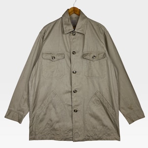 K&ouml;nnte beinhalten: Beigefarbene Jacke mit Knopfleiste, zwei Brusttaschen und zwei unteren Taschen. Die Jacke h&auml;ngt an einem Holzb&uuml;gel. Die Jacke hat einen Kragen und lange &Auml;rmel.